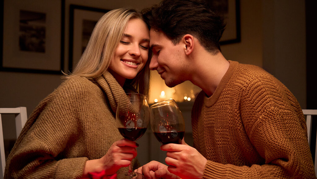 romantic dinner ideas with a happy couple in love clinking glasses drinking red wine at home.