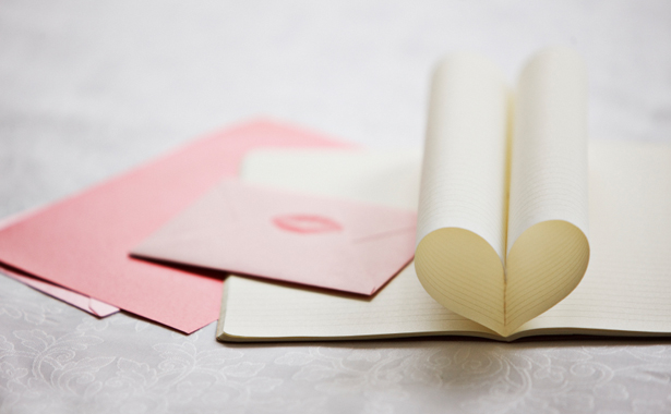 Close up of lipstick kiss on envelope and pages of notebook forming heart-shape