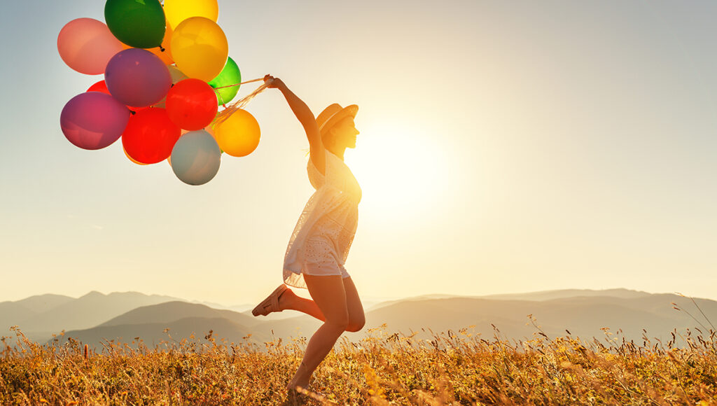 July birthdays with a woman with balloons at sunset in summer