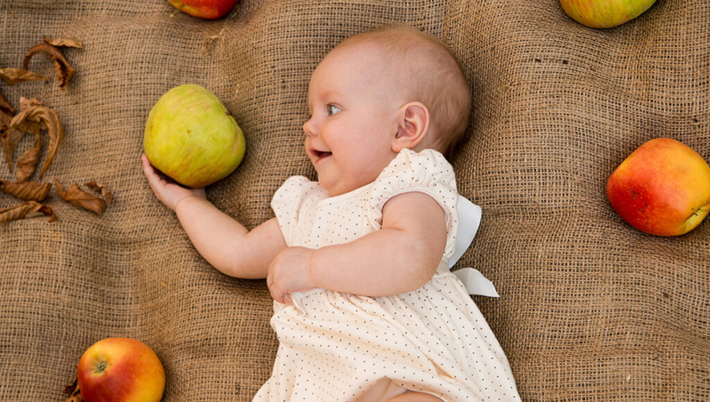 September birthdays with a cute baby girl laying next to apples.