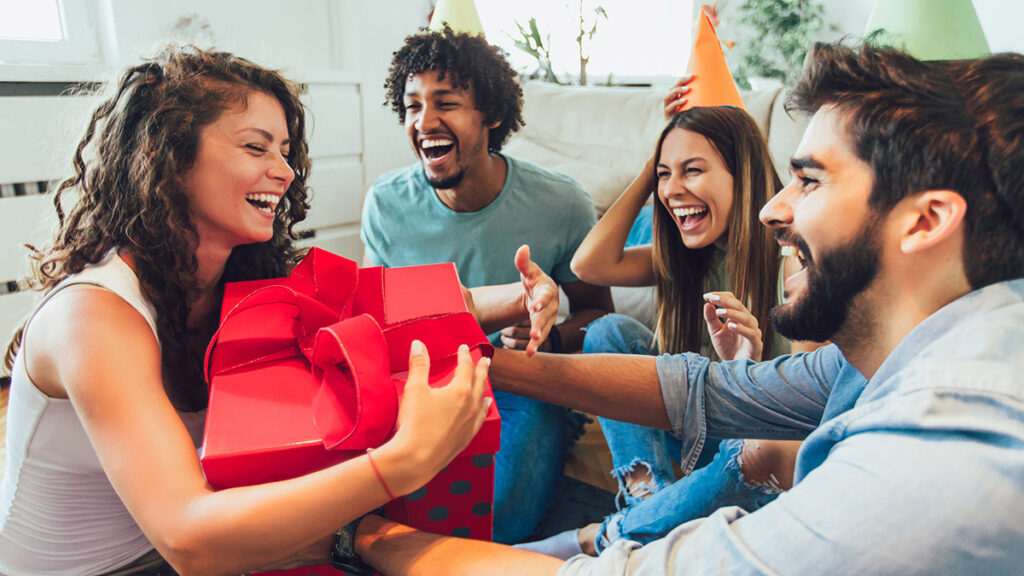 birthday gifts for libra woman holding a big red box surrounded by friends at a birthday party.