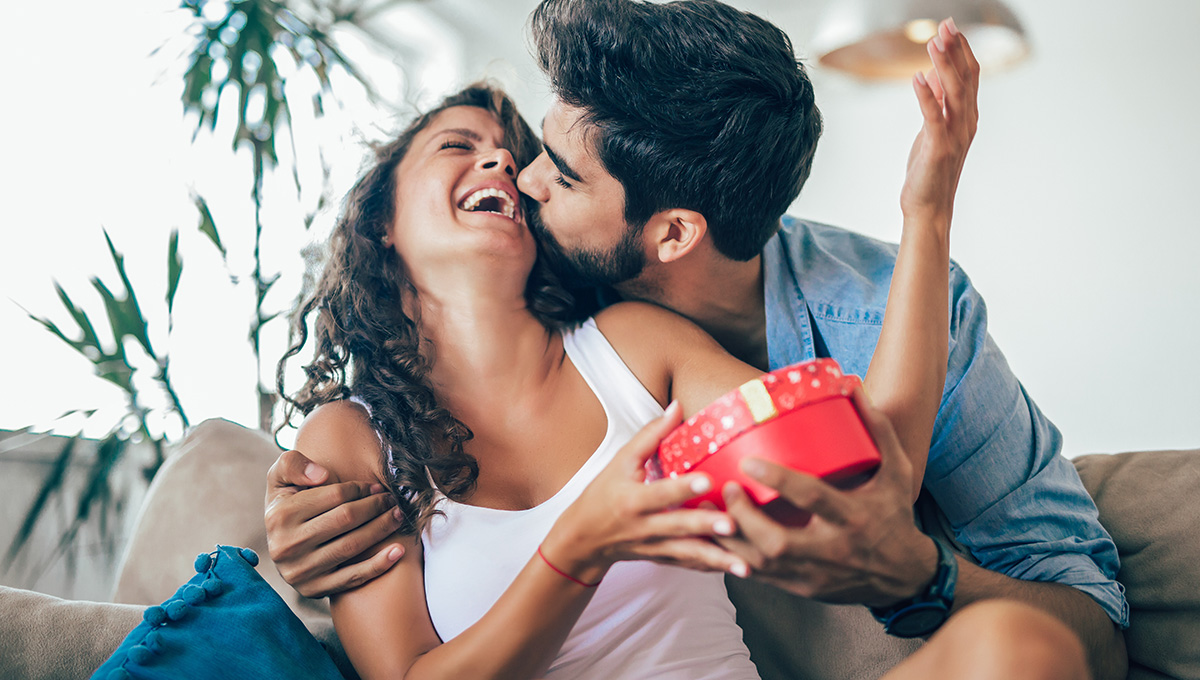 A photo of a gift giver giving a surprise gift to woman at home.