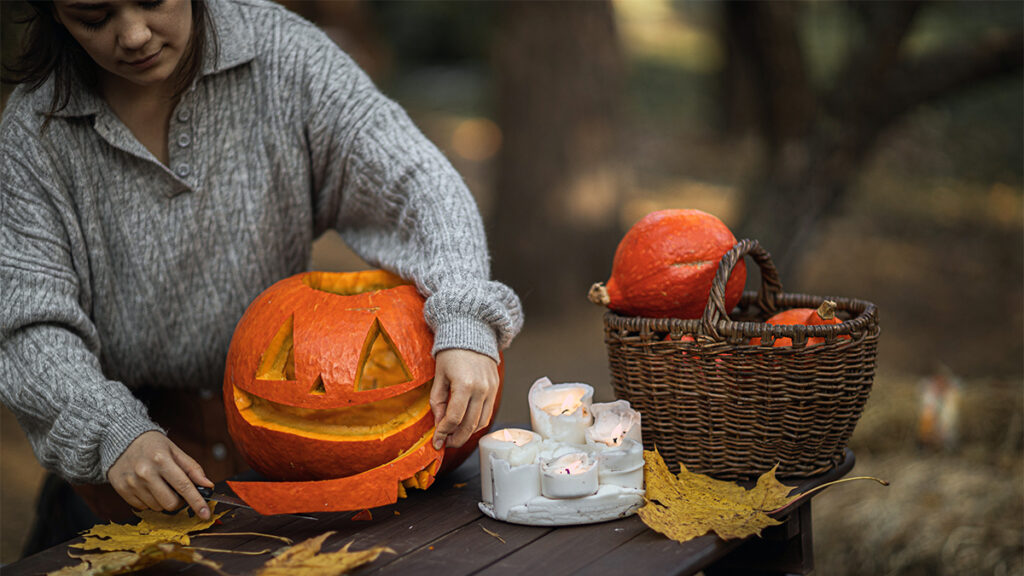 history of halloween woman carving a pumpkin on a wooden table outdoors.