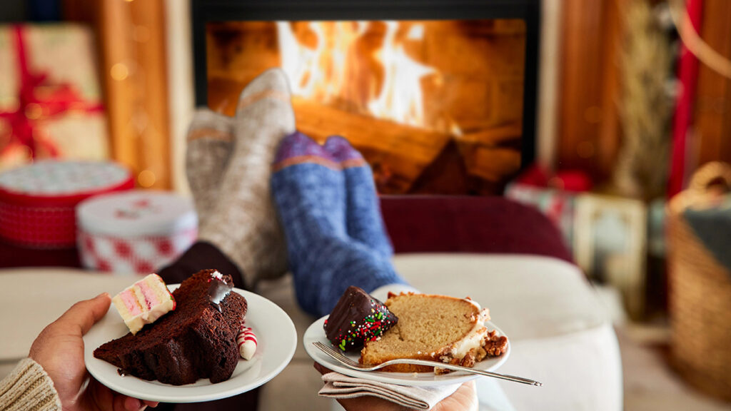 winter gifts couple lounging in front of fireplace with dessert.